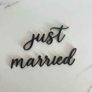 May include: Black cursive text that reads "just married" on a white marble surface. The words are separate and in a stylish font, perfect for wedding decor or photo props.