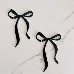 May include: Two black bow shapes cut from acrylic. The bows are simple and elegant.