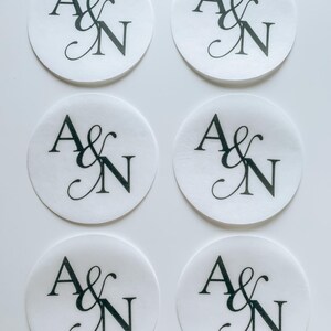 May include: Six white, circular stickers with the letters "A & N" in black script. The stickers are arranged in two rows of three, with the text centered on each sticker. The background is plain white.