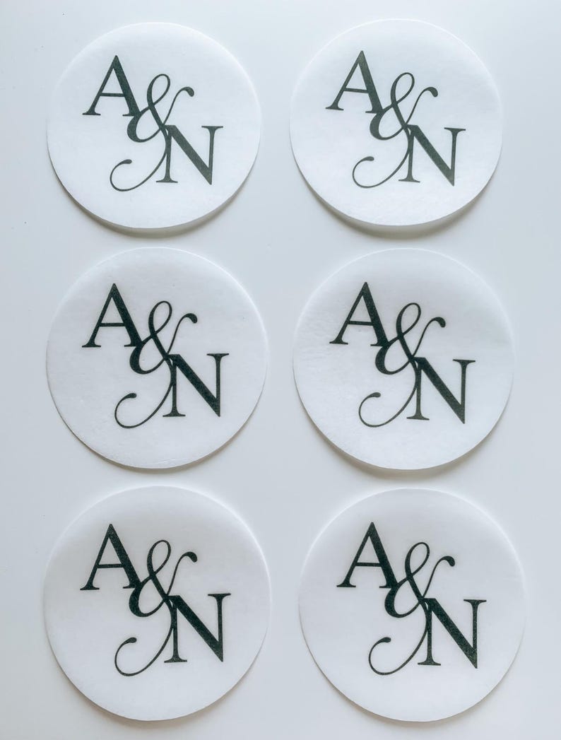 May include: Six white, circular stickers with the letters "A & N" in black script. The stickers are arranged in two rows of three, with the text centered on each sticker. The background is plain white.