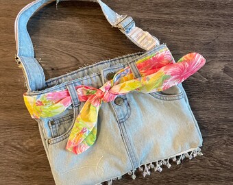 May include: A light blue denim bag with a floral print scarf tied around the top. The bag has a beaded trim and a long strap.