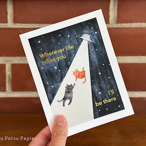 Close up of greeting card of hand painted illustration of two cats sitting on a fence and looking up at the moon. Message and embellishments in gold pressed-foil.