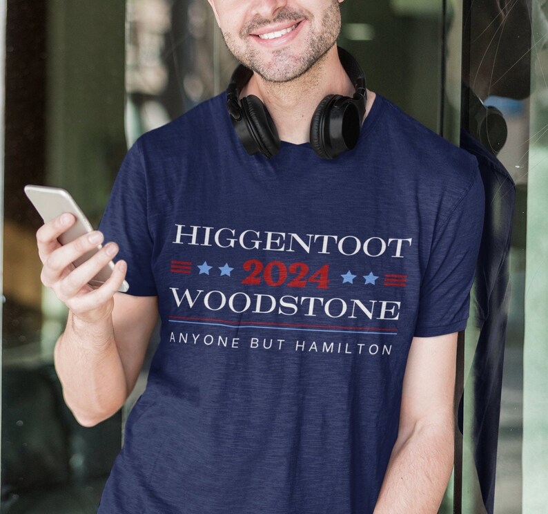Op de afbeelding: Een marineblauw t-shirt met de tekst "Higgentoot 2024 Woodstone Anyone But Hamilton" gedrukt in wit, rood en blauw.