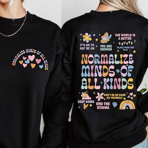 May include: Black sweatshirt with a rainbow-colored graphic that says "Normalize Minds of All Kinds" and includes other positive messages like "It's OK to not be OK", "You are enough", "Keep Going", "Don't be so hard on yourself", and "End the Stigma".