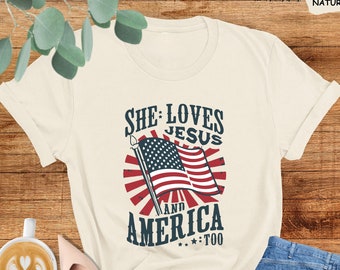 May include: A beige t-shirt with a graphic design featuring an American flag and the text "She Loves Jesus and America Too".