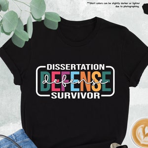 May include: Black t-shirt with the text "Dissertation Defense Survivor" in colorful letters. The text is inside a white rectangle with a black border.