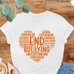 May include: White t-shirt with the words "END BULLYING" in orange, arranged in a heart shape. The heart is filled with words like "friendship", "kindness", and "courage". The shirt is paired with blue jeans and nude-colored shoes.