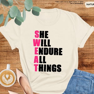 May include: A white t-shirt with the words "SHE WILL ENDURE ALL THINGS" printed in black with the word "SWEAT" in pink.