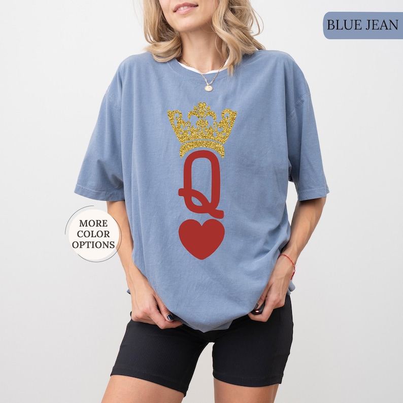 May include: A blue jean t-shirt with a gold glitter crown and a red heart with the letter Q in the middle. The text "MORE COLOR OPTIONS" is in a white box on the left side of the image. The text "BLUE JEAN" is in a white box on the right side of the image.