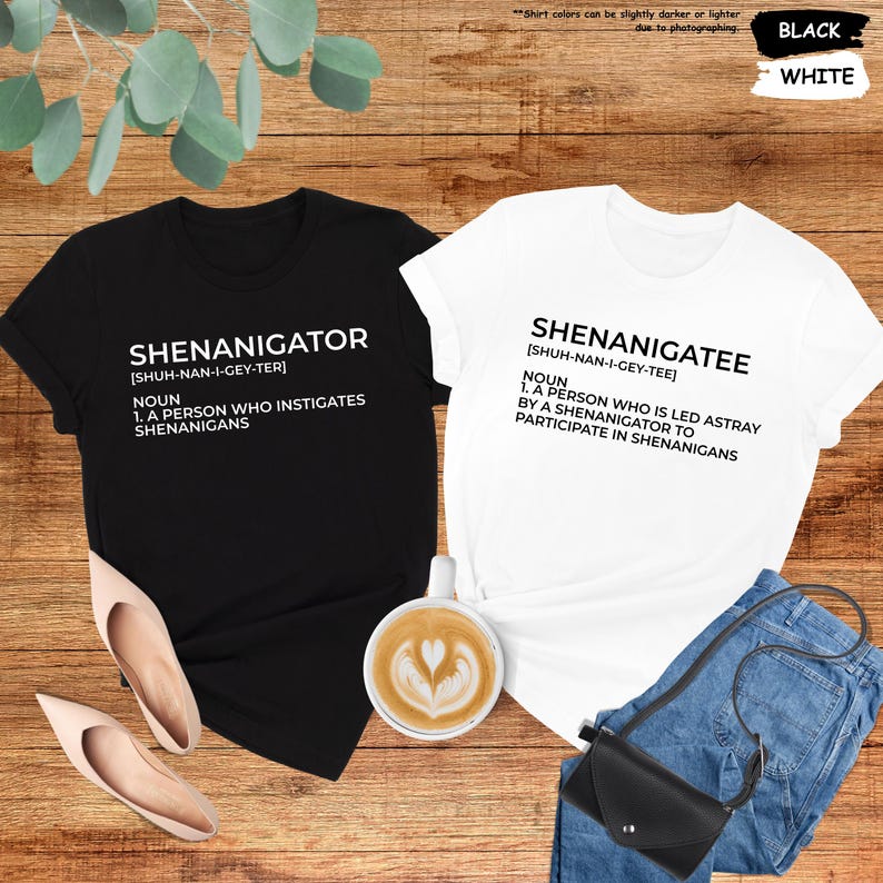 Pode incluir: Duas camisetas pretas e brancas com uma defini&ccedil;&atilde;o das palavras "Shenanigator" e "Shenanigatee". As camisetas est&atilde;o dispostas sobre uma superf&iacute;cie de madeira com uma x&iacute;cara de caf&eacute;, um par de sapatos e uma bolsa.