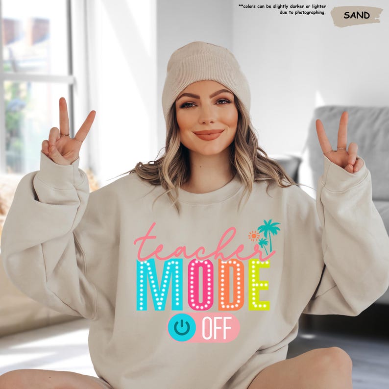 May include: A light beige sweatshirt with the text "teacher mode off" in colorful letters. The text is surrounded by a colorful light bulb and palm trees.