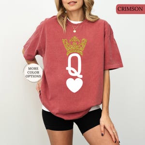 May include: A red t-shirt with a white queen of hearts design and a gold glitter crown. The text "CRIMSON" is in the top right corner of the image.