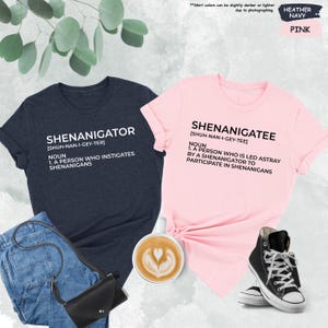 Pode incluir: Duas t-shirts com uma defini&ccedil;&atilde;o das palavras "Shenanigator" e "Shenanigatee". A camiseta &agrave; esquerda &eacute; azul marinho mesclado e a camiseta &agrave; direita &eacute; rosa.