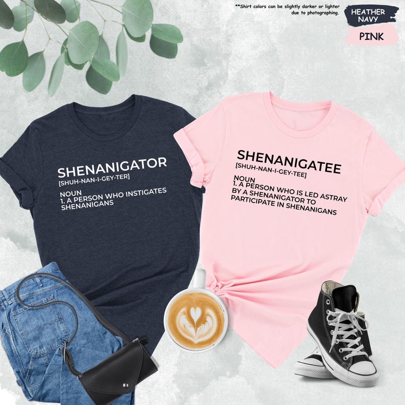Pode incluir: Duas t-shirts com uma defini&ccedil;&atilde;o das palavras "Shenanigator" e "Shenanigatee". A camiseta &agrave; esquerda &eacute; azul marinho mesclado e a camiseta &agrave; direita &eacute; rosa.