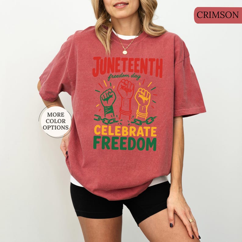 K&ouml;nnte beinhalten: Karmesinrotes T-Shirt mit den Worten "Juneteenth freedom day" und "Celebrate Freedom" in Rot, Gelb und Gr&uuml;n. Das Shirt zeigt drei erhobene F&auml;uste in Gr&uuml;n, Rot und Gelb, mit Ketten und Armb&auml;ndern.