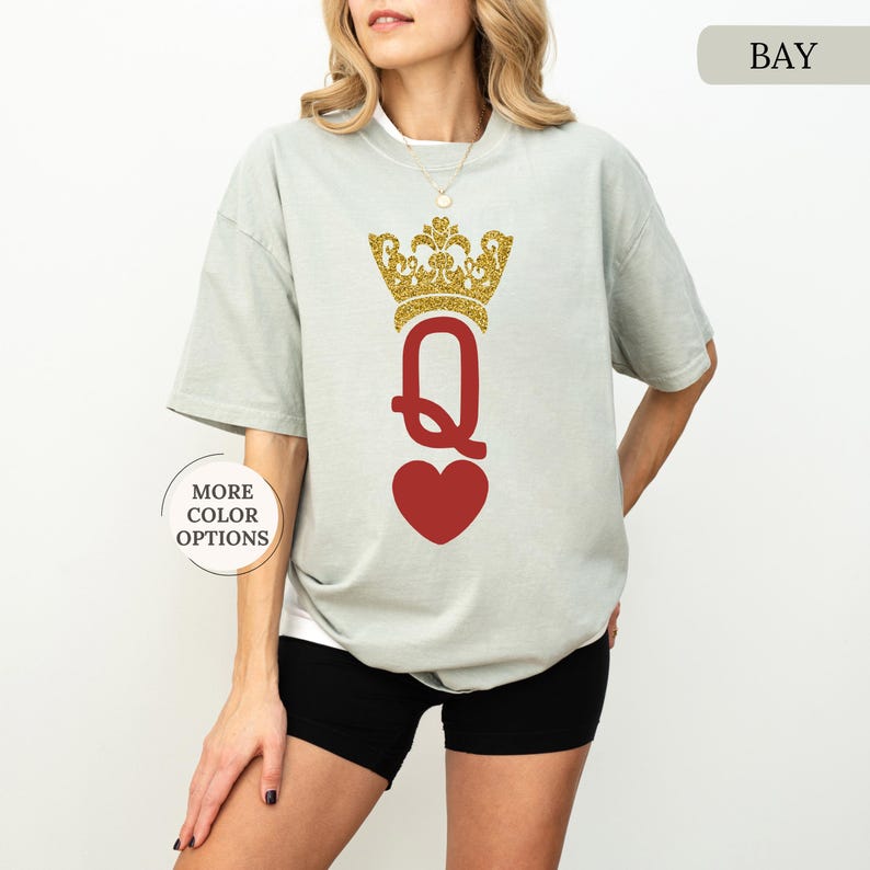 May include: A light gray t-shirt with a red heart and a gold glitter crown above the letter "Q". The text "BAY" is in the upper right corner of the image.