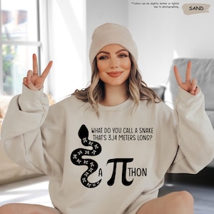 May include: A beige sweatshirt with a black snake design and the text "What do you call a snake that's 3.14 meters long? A Pi-thon".