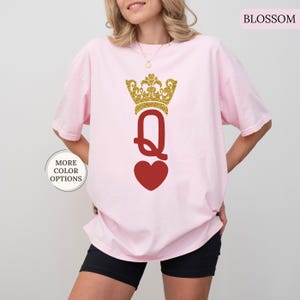 May include: A pink t-shirt with a gold glitter crown and a red heart with a gold glitter "Q" in the center. The text "BLOSSOM" is in the upper right corner of the image.
