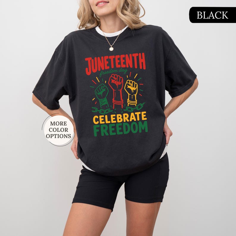K&ouml;nnte beinhalten: Schwarzes T-Shirt mit den Worten "Juneteenth freedom day" in Rot und Gr&uuml;n sowie "Celebrate Freedom" in Gelb und Gr&uuml;n. Das Shirt zeigt drei erhobene F&auml;uste in Gr&uuml;n, Rot und Gold. Die Worte "More Color Options" sind sichtbar.