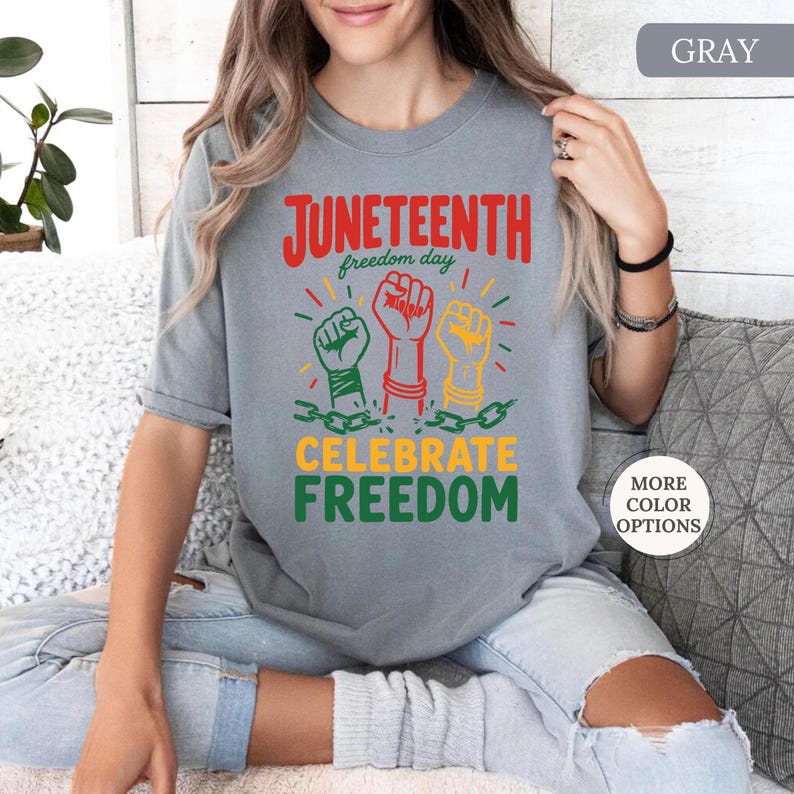 K&ouml;nnte beinhalten: Graues T-Shirt mit den Worten "Juneteenth freedom day" in Rot und Gr&uuml;n. Das Shirt zeigt drei erhobene F&auml;uste in Gr&uuml;n, Rot und Gelb, mit den Worten "Celebrate Freedom" darunter.