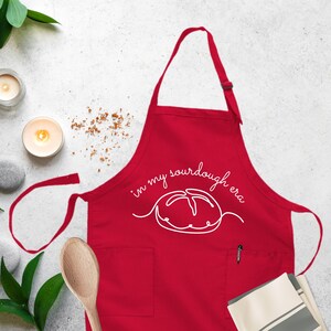 Puede incluir: Delantal de cocina rojo con un contorno blanco de una hogaza de pan de masa madre y el texto "in my sourdough era".