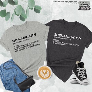 Pode incluir: Duas camisetas com uma defini&ccedil;&atilde;o das palavras "Shenanigatee" e "Shenanigator". As camisetas s&atilde;o de cor cinza mescla e cinza mescla escuro.