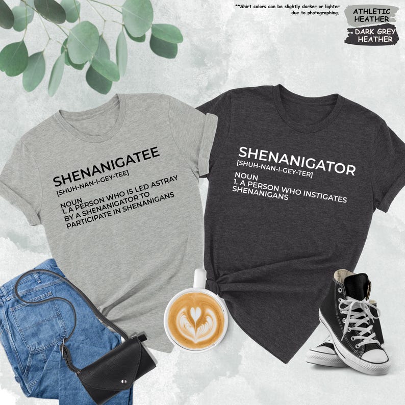 Pode incluir: Duas camisetas com uma defini&ccedil;&atilde;o das palavras "Shenanigatee" e "Shenanigator". As camisetas s&atilde;o de cor cinza mescla e cinza mescla escuro.