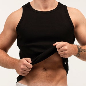 May include: A black ribbed tank top with a scoop neck. The tank top is being held up by a person's hand.