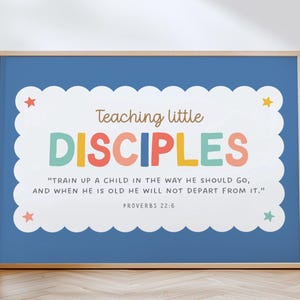 Puede incluir: Una impresión enmarcada con un fondo azul y un borde blanco festoneado. El texto dice "Teaching little DISCIPLES" en letras coloridas, con un versículo bíblico debajo. Estrellas decorativas están colocadas alrededor del borde. El marco es de color madera clara.