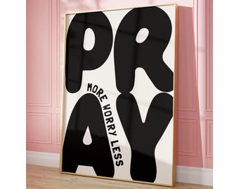 May include: A rectangular wall art print in a light wood frame featuring a white background with large, bold black letters spelling PRAY. The words MORE WORRY LESS are printed in smaller black sans-serif font between the letters P and R.