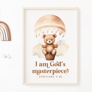 Puede incluir: Un oso de peluche marrón en un globo aerostático con una cubierta a rayas blancas y marrones. El globo flota sobre una nube blanca. El texto "Soy la obra maestra de Dios" y "Efesios 2:10" está debajo del globo.