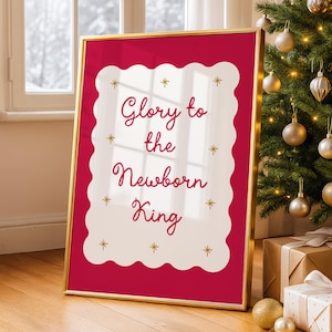 Puede incluir: Una impresión enmarcada con el texto "Glory to the Newborn King" en una escritura decorativa. El marco es dorado y el fondo es rojo intenso. La impresión está decorada con estrellas doradas y se exhibe cerca de un árbol de Navidad.
