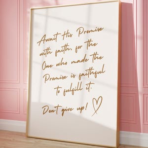 Puede incluir: Una impresión en lienzo blanco con una cita dorada que dice "Await His Promise with faith, for the One who made the Promise is faithful to fulfill it. Don't give up!" con un símbolo de corazón dorado.