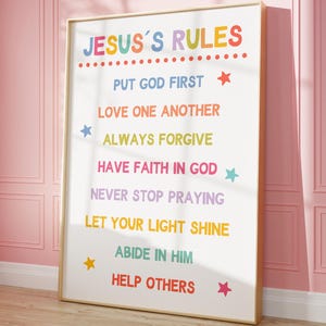 以下が含まれることがあります： 虹色の文字で「JESUS'S RULES」と書かれた、金色の額縁が付いた白いポスター。ポスターには、「神を第一に置く」「互いに愛し合う」「常に許す」「神を信じる」「祈り続ける」「光を輝かせる」「彼の中に留まる」「他人を助ける」など、人生の指針となるルールが書かれています。