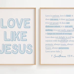 May include: Two framed prints with light blue text on a white background. One print says "LOVE LIKE JESUS" in large letters. The other print features a Bible verse from 1 Corinthians 13:4-8 about love. The frames are a light wood color.