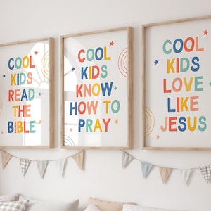 Puede incluir: Tres impresiones artísticas enmarcadas con las frases "COOL KIDS READ THE BIBLE", "COOL KIDS KNOW HOW TO PRAY" y "COOL KIDS LOVE LIKE JESUS" en texto colorido. Cada impresión tiene un marco de madera y está decorada con estrellas y arcoíris.