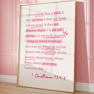 May include: A framed print with a gold border displays the text "Love is patient, love is kind" from 1 Corinthians 13:4-8. The words are in black, with some highlighted in pink. The background is a soft white.