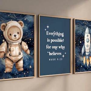 Puede incluir: Tres impresiones enmarcadas con un tema espacial. La primera impresión presenta un oso de peluche marrón con un traje de astronauta sobre un cielo estrellado azul. La segunda impresión tiene un fondo azul con texto blanco que dice "Todo es posible para el que cree MARCOS 9:23". La tercera impresión presenta un cohete blanco con llamas naranjas sobre un cielo estrellado azul.