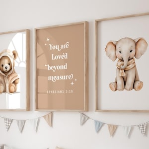 Puede incluir: Tres impresiones enmarcadas con fondo beige. La impresión de la izquierda presenta un oso de peluche marrón que lleva una bata con capucha marrón. La impresión del medio presenta un fondo beige con el texto "You are loved beyond measure" y "Ephesians 3:19". La impresión de la derecha presenta un elefante marrón claro que lleva una bufanda marrón.