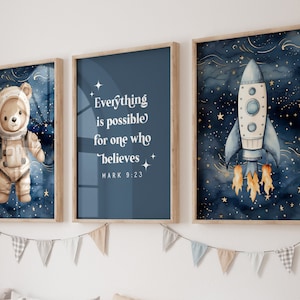 Puede incluir: Tres impresiones enmarcadas con fondo azul y estrellas doradas. La impresión de la izquierda presenta un osito de peluche con un traje de astronauta. La impresión del medio tiene el texto "Todo es posible para el que cree MARCOS 9:23". La impresión de la derecha muestra un cohete con llamas.