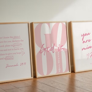 Puede incluir: Tres impresiones artísticas enmarcadas con citas inspiradoras en escritura rosa sobre fondo blanco. Las impresiones están en marcos de madera clara y se apoyan contra una pared. Las citas incluyen "Dios es todo el tiempo" y versículos bíblicos.