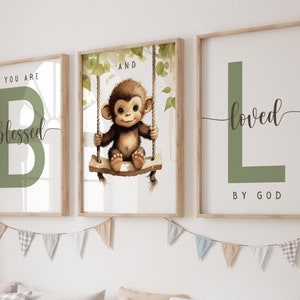 Puede incluir: Tres impresiones enmarcadas con una letra verde, un mono en un columpio y una letra verde con la palabra "loved" en cursiva. Las impresiones incluyen las palabras "You are blessed" y "And loved by God".