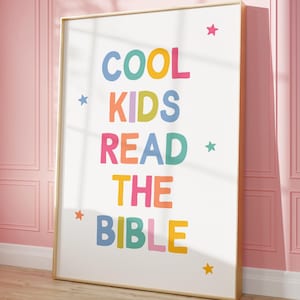 Puede incluir: Un póster enmarcado con el texto "COOL KIDS READ THE BIBLE" en letras coloridas y divertidas. Las palabras están dispuestas verticalmente sobre un fondo blanco, con acentos de estrellas. El marco es de color madera clara.