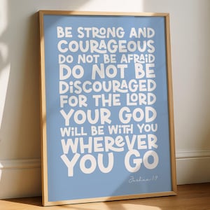 Könnte beinhalten: Ein gerahmter Kunstdruck mit hellblauem Hintergrund und weißem Text: BE STRONG AND COURAGEOUS DO NOT BE AFRAID DO NOT BE DISCOURAGED FOR THE LORD YOUR GOD WILL BE WITH YOU WHEREVER YOU GO, mit der Inschrift Joshua 1:9 am unteren Rand des Bildes.