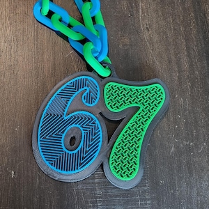 May include: A blue and green chain necklace with a pendant featuring the number "67". The pendant has a black base with blue and green accents. The chain is a mix of blue and green links.
