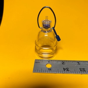以下が含まれることがあります： 銀色のハンドルと青いキャップが付いた、小さな透明なガラス瓶。 ボトルは水平の溝がある円筒形をしています。 ボトルの横には定規が置かれ、センチメートル単位の測定値が表示されています。