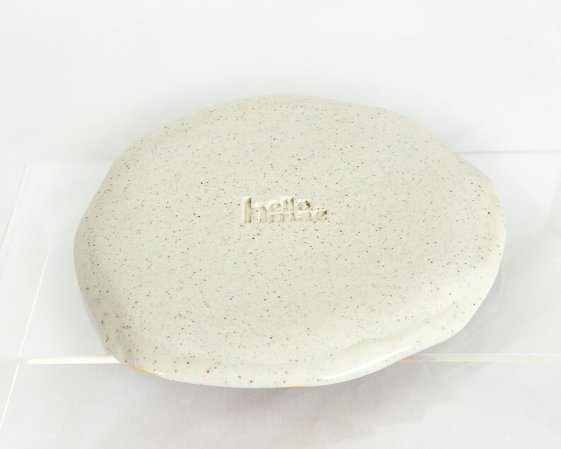 13.5cm ceramic mini plate with check design. Colours are yellow, pink,blue and green on white speckled clay.Bottom of the plate shows the hellomaë branded stamp.
