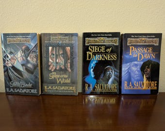 May include: Four paperback fantasy novels with black and white covers featuring illustrations of characters and text that reads "Forgotten Realms" and "R.A. Salvatore". The titles of the books are "The Spine of the World", "Siege of Darkness", "Passage to Dawn", and "Silth Blade".