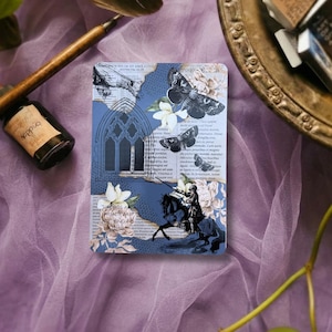 May include: A rectangular card featuring a collage of vintage newspaper text, a blue gothic archway, black moth illustrations, white flowers, and a silhouette of a knight on horseback with the text "Swords and armor are nothing to stone."