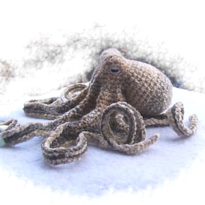May include: A crocheted octopus with brown and white yarn. The octopus is lying on a white surface.